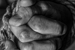 A hand folded together in close-up photography, in black and white, with a soft focus on the fingers and hand.