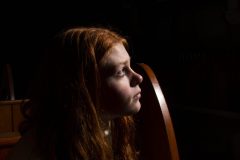 “Fine art portrait of young woman with beautiful red hair in a minimal setting, focusing on stillness, light, and presence.”
